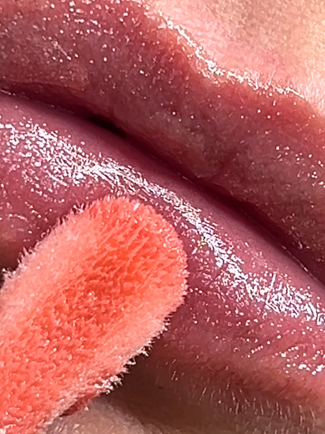 Close up image of lips wearing e.l.f Glow Reviver Lip Oil Glimmer in the shade "Princess Cut", showing pink tint and glitter detail as the applicator touches the bottom lip; beauty lip product application.