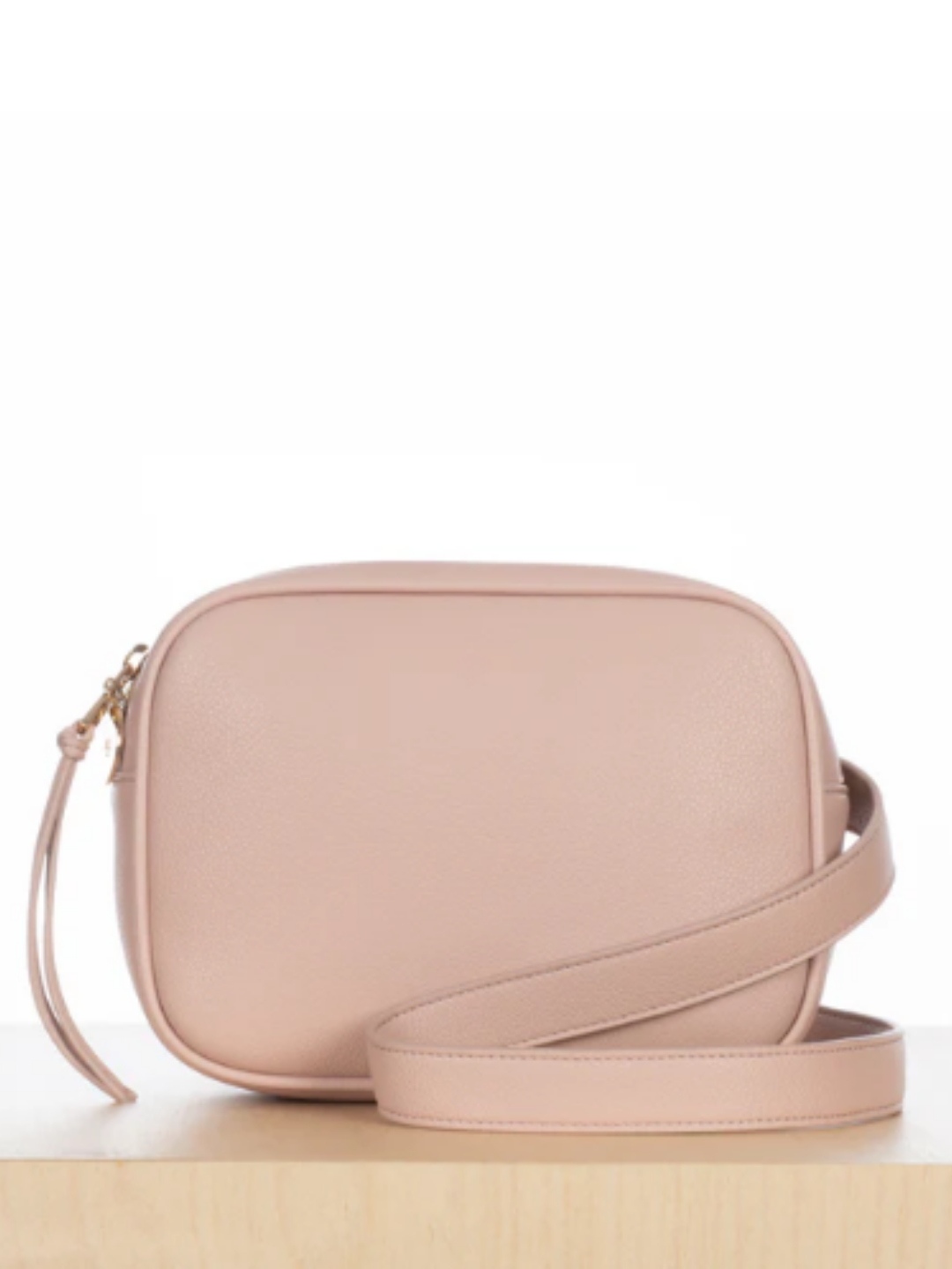 Pink Ela belt bag displayed on a white background and resting on a wooden surface, with the strap folded forward to show its shape and detailing.