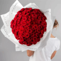 A young white woman with a messy bun holding an oversized bouquet of about 200 roses wrapped in Appleyard London wrapping paper, her face hidden behind the blooms, creating a soft moment of floral luxury and self-care.