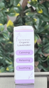 Side of Plant Therapy Organic Lavender Pure Essential Oil box in white packaging with purple trim, shown outdoors on a table with lattice and ivy in the background. The side panel features lavender illustrations at the top and bottom, and text that reads 'Get to Know Organic Lavender" with three stacked oblong purple shapes labeled "Calming", "Relaxing", "Soothing".