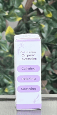 Side of Plant Therapy Organic Lavender Pure Essential Oil box in white packaging with purple trim, shown outdoors on a table with lattice and ivy in the background. The side panel features lavender illustrations at the top and bottom, and text that reads 'Get to Know Organic Lavender" with three stacked oblong purple shapes labeled "Calming", "Relaxing", "Soothing".