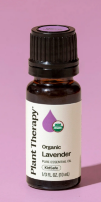 Plant Therapy Organic Lavender Pure Essential Oil bottle on a purple surface with a purple background. The brown bottle has a black twist-off cap, a white label with a purple essential oil drop, a circular USDA Organic label, and text reading "Organic Lavender Pure Essential Oil, Kid Safe' along with the fluid ounces and milliliters in the bottle.