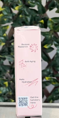 Side view of Plant Therapy Rose with Bakuchiol Facial Serum box in light pink packaging with white floral accents, shown outdoors on a table with lattice and ivy in the background. The side panel reads "Restore Radiance", "Anti-Aging", and "Hello Hydration", with cute illustrations of a smiling sun, an hourglass, and a squiggly line, plus a QR code labeled "Get the full story here".