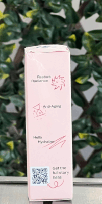 Side view of Plant Therapy Rose with Bakuchiol Facial Serum box in light pink packaging with white floral accents, shown outdoors on a table with lattice and ivy in the background. The side panel reads "Restore Radiance", "Anti-Aging", and "Hello Hydration", with cute illustrations of a smiling sun, an hourglass, and a squiggly line, plus a QR code labeled "Get the full story here".