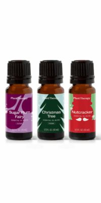 Three brown glass essential oil bottles with black caps from Plant Therapy Christmas Magic Essential Oil Blend 3 set. The first bottle, labeled "Christmas Tree", has a light blue snow-themed packaging with a green Christmas tree. The second, "Nutcracker", has a green label with a red nutcracker outline and white mustache. The third, "Sugar Plum", features a light purple label with a deep purple plum design.
