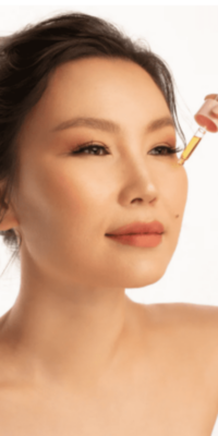 Asian woman applying OYU Botanica Bakuchiol Booster Serum to her face against a white background, demonstrating skincare application.