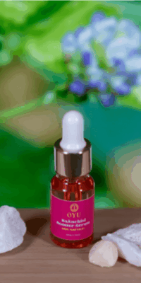 OYU Botanica Bakuchiol Booster Serum bottle diplayed on a wooden surface, surrounded by crystals, with an unfocused image of bakuchiol plant in the background.