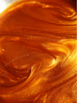 Golden Hour Glow Body Oil by Ancient Owl Naturals spread across a smooth surface, revealing its radiant bronze shimmer and luminous texture that evokes warmth, confidence, and self-love.