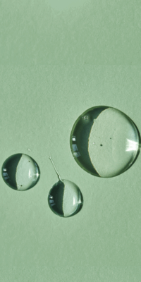 Three drops of squalene resting on a green background, a key ingredient in this Bakuchiol serum.