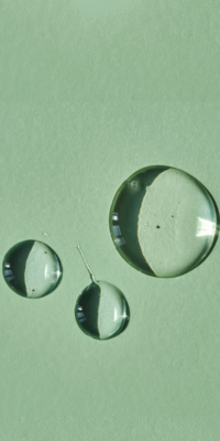 Three drops of squalene resting on a green background, a key ingredient in this Bakuchiol serum.